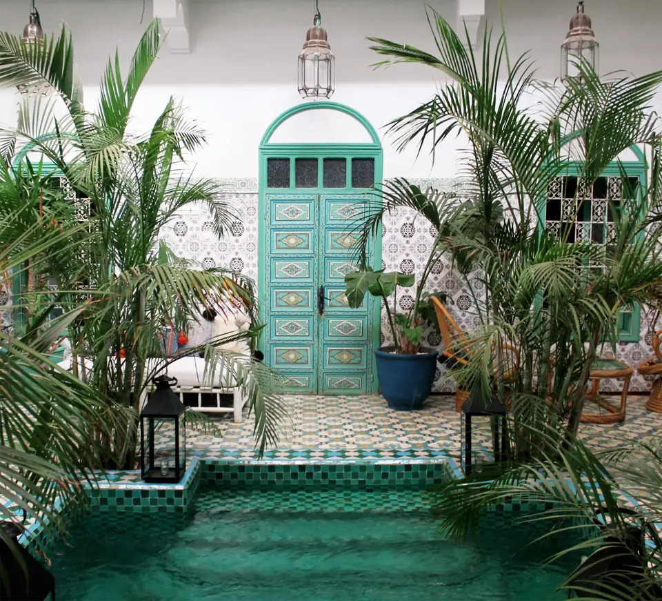 Patio de riad habillé de zellige vert et blanc, porte peinte et palmiers en pot